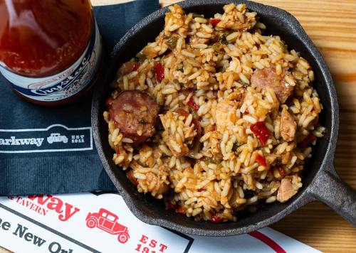 A cast iron skillet filled with flavorful rice and sausage, accompanied by a bottle of soda on a wooden table.