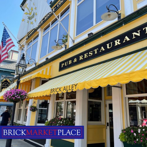 Exterior of a pub and restaurant with yellow awnings, flowers, and American flags at Brick Marketplace.
