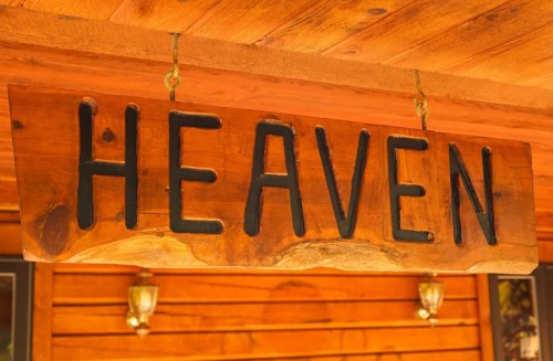 Wooden sign with the word "HEAVEN" carved in bold black letters, hanging from a rustic wooden ceiling.
