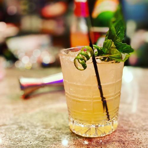 A refreshing cocktail in a glass, garnished with a sprig of mint and a twist of lime, on a bar countertop.