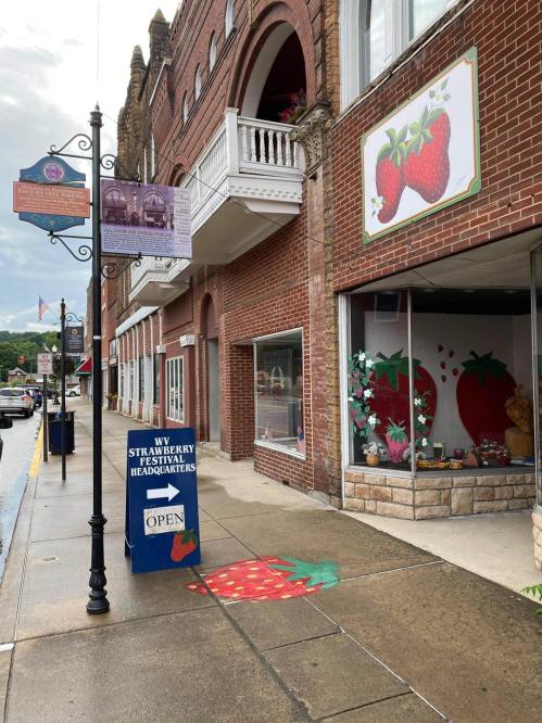 A street view of a brick building with strawberry-themed decorations and a sign for the Strawberry Festival Headquarters.