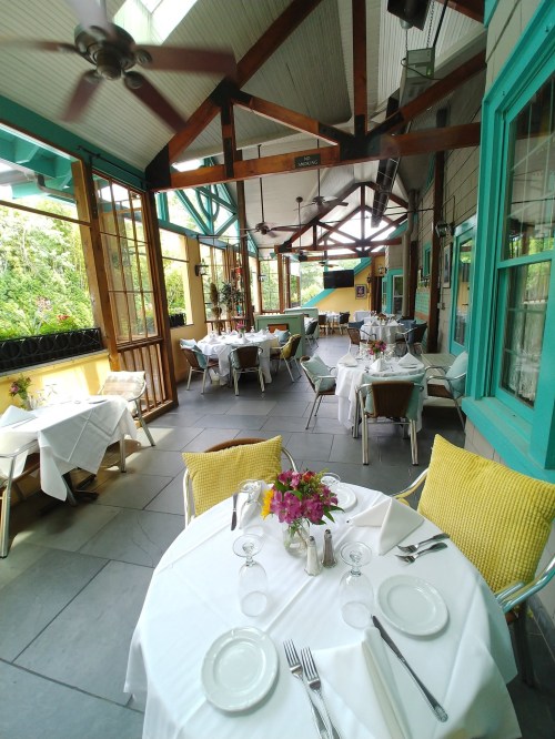 A bright, airy restaurant with tables set for dining, featuring large windows and tropical decor.