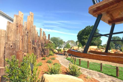 A scenic garden path lined with greenery and wooden structures under a clear blue sky.