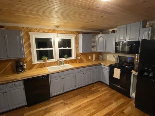 A cozy kitchen with light blue cabinets, wooden accents, and modern appliances, featuring a sink and wooden flooring.
