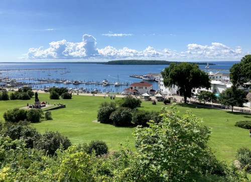 A scenic view of a marina with boats, lush green park, and blue sky with clouds in the background.
