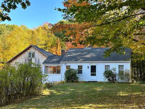 A charming white house surrounded by colorful autumn trees and greenery on a sunny day.