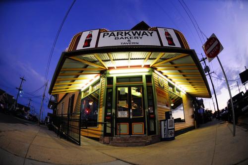 A brightly lit corner building with a sign reading "Parkway Bakery & Tavern" at dusk.