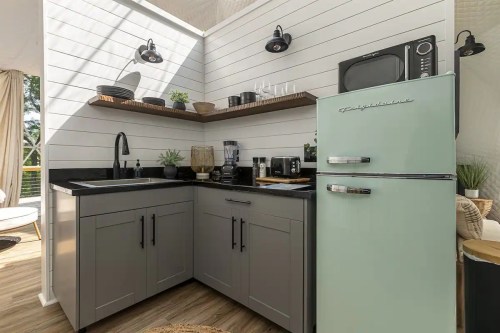 Modern kitchen corner with gray cabinets, black countertops, a mint green fridge, and various appliances on shelves.