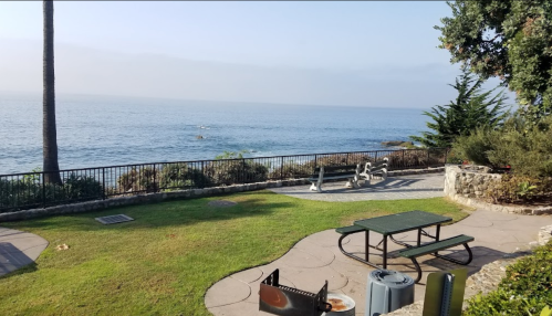 A serene coastal view with a grassy area, picnic table, and ocean in the background under a clear sky.