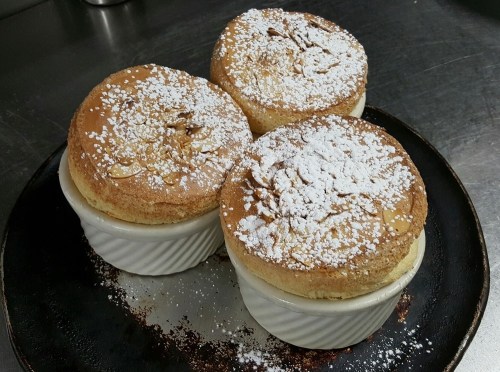 Three golden soufflés dusted with powdered sugar, served in white ramekins on a black plate.