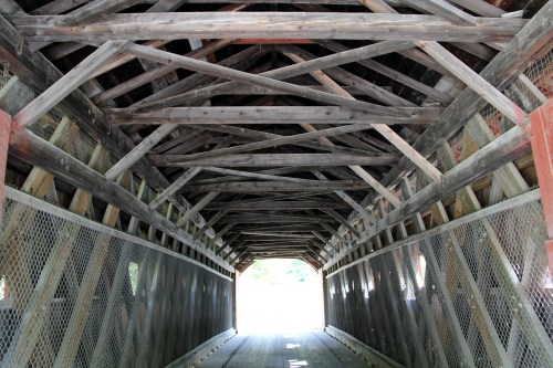 Interior view of a covered bridge, showcasing wooden beams and a light-filled exit at the far end.