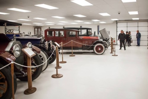 A vintage car exhibit featuring classic cars, with visitors observing in a well-lit gallery.