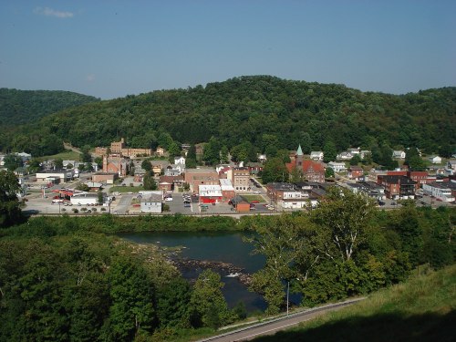 A scenic view of a small town nestled by a river, surrounded by green hills under a clear blue sky.