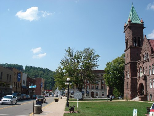 A scenic view of a small town with historic buildings, a clock tower, and a tree-lined street under a clear blue sky.