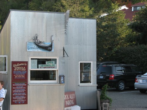 A small, silver food stand with a sign reading "Gondola" and a parking area nearby. Trees in the background.