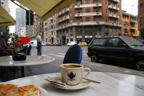 A coffee cup on a table with a view of a city street and buildings in the background.