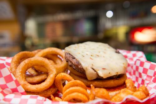 A juicy cheeseburger with melted cheese on a bun, served with curly fries and onion rings in a red-checkered basket.