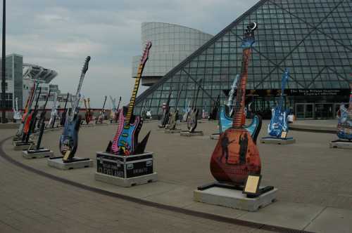 Colorful, oversized guitars displayed outdoors near a modern glass building, showcasing artistic designs.