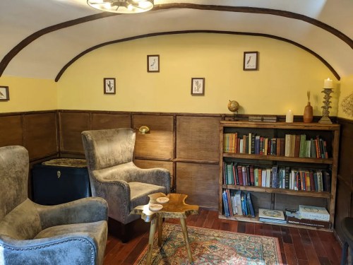 Cozy room with two armchairs, a wooden bookshelf filled with books, and warm yellow walls. A small table and decor complete the space.