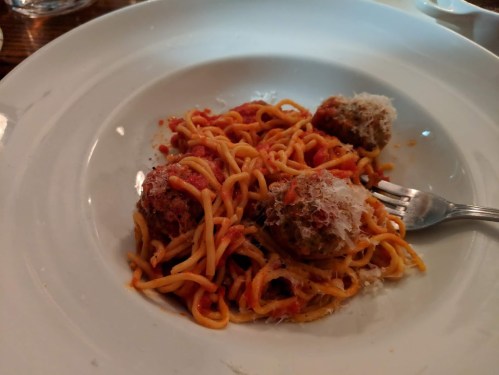 A plate of spaghetti with meatballs, topped with grated cheese, served with a fork on the side.