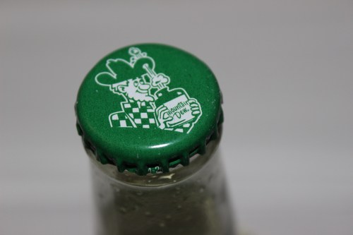 Green bottle cap featuring a cartoon cowboy holding a drink, with the text "Mountain Dew."