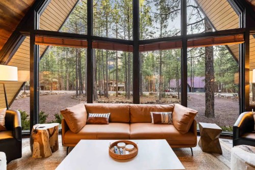Cozy living room with a brown sofa, large windows showcasing a forest view, and modern decor.