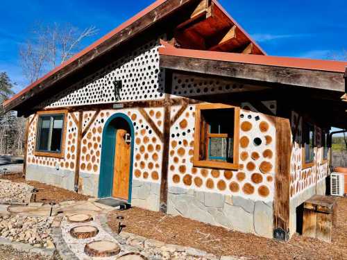 A unique house with a dotted exterior, wooden accents, and a stone pathway, set against a clear blue sky.