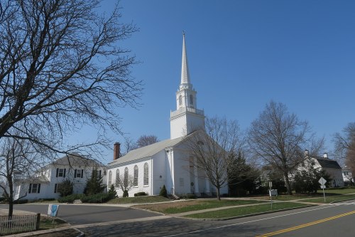 A white church with a tall steeple, surrounded by bare trees and a clear blue sky.