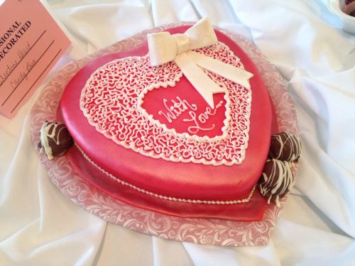 A heart-shaped cake decorated with pink icing, a white bow, and the words "With Love" in the center.