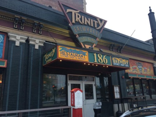 Exterior of Trinity Brewhouse, featuring a colorful sign and entrance, with a vintage fire alarm box nearby.