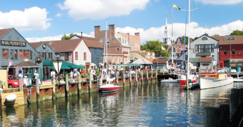 A picturesque waterfront scene with colorful buildings, boats, and people enjoying a sunny day by the water.