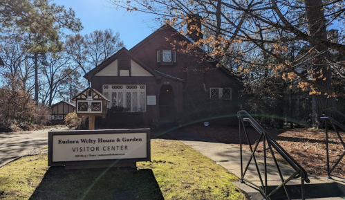 A brick house with a sign reading "Eudora Welty House & Garden Visitor Center" surrounded by trees.