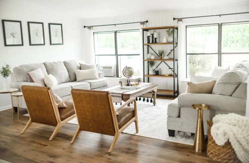 Bright living room with gray sofas, wooden chairs, a coffee table, and large windows, featuring a cozy, modern decor.