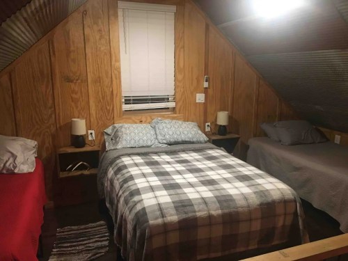 Cozy attic bedroom with wooden walls, a double bed with a plaid blanket, and two side tables with lamps.