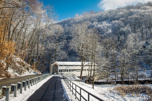 A snow-covered landscape with a path leading to a white building, surrounded by trees and a blue sky.
