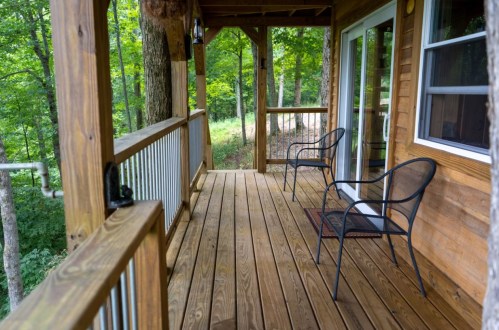 A wooden porch with two black chairs, surrounded by lush green trees and a peaceful outdoor setting.