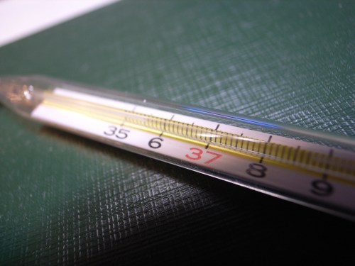 Close-up of a glass thermometer showing a temperature reading of 37 degrees Celsius on a textured green background.