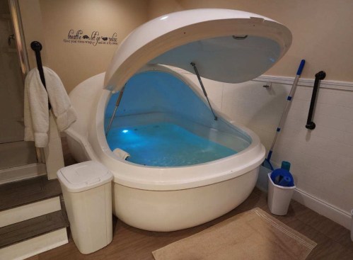 A futuristic floatation tank with a blue interior, partially open, in a serene bathroom setting.