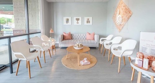 A modern waiting area with white chairs, a round table, and decorative art on the walls, featuring soft pink accents.