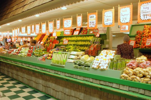 A vibrant grocery store display filled with fresh fruits and vegetables, with colorful price signs and shoppers browsing.