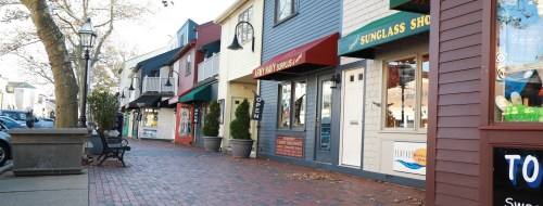 A charming street lined with colorful shops and a brick walkway, featuring a "Sunglass Shop" and outdoor seating.