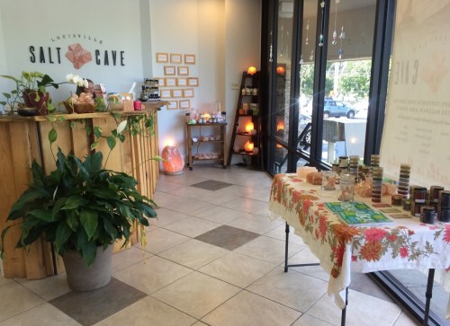 Interior of a salt cave spa with a reception desk, candles, and a table displaying products. Warm, inviting atmosphere.