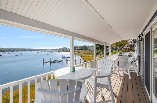 A scenic view from a porch overlooking a calm bay with boats and autumn foliage in the background.