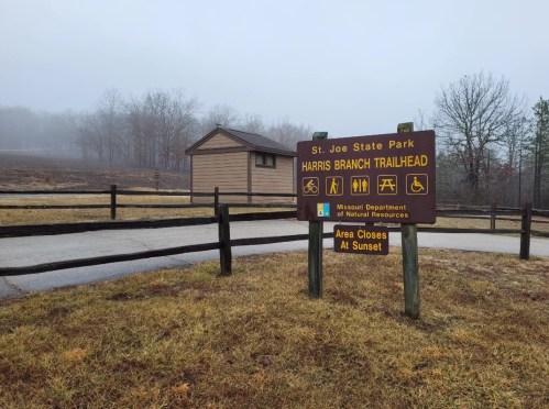 Sign for Harris Branch Trailhead at St. Joe State Park, surrounded by foggy landscape and wooden fencing.