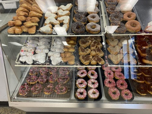 A display case filled with various donuts, including glazed, powdered, and decorated options in different shapes.