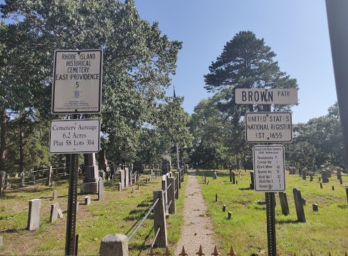 A cemetery path with signs indicating "Brown Path" and historical information about the site in East Providence, Rhode Island.