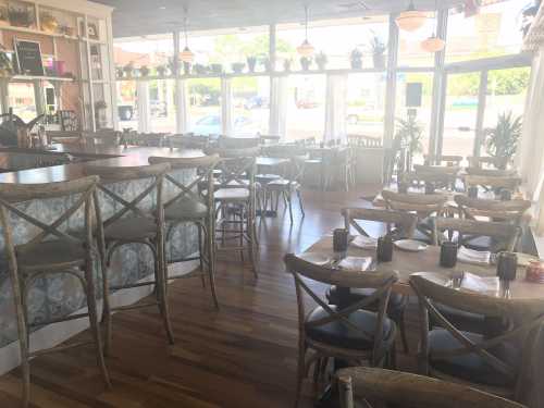 Bright restaurant interior with wooden floors, tables set for dining, and large windows letting in natural light.