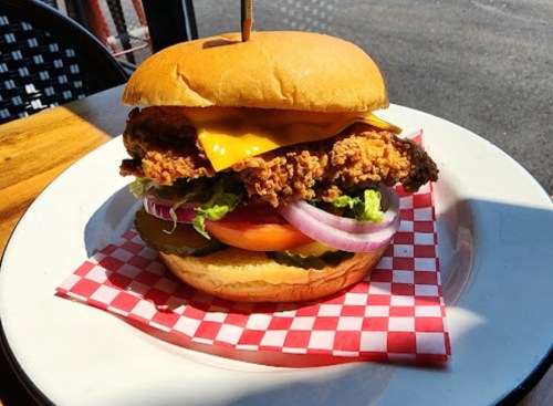 A crispy chicken burger with cheese, lettuce, tomato, and onion on a toasted bun, served on a checkered paper.