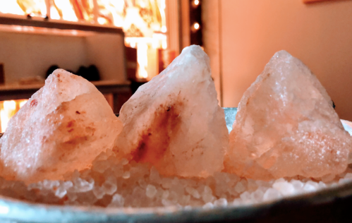 Three large, irregularly shaped salt crystals on a bed of smaller salt grains, with warm lighting in the background.