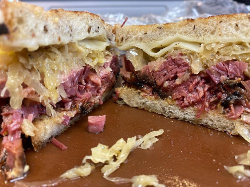 Close-up of a sliced sandwich filled with layers of corned beef, sauerkraut, and melted cheese on rye bread.